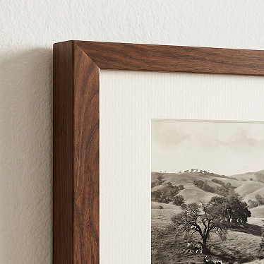 Close-up of a framed landscape photograph showing a dark brown wood frame, white mat board, and a black-and-white scenic print of rolling hills and trees.