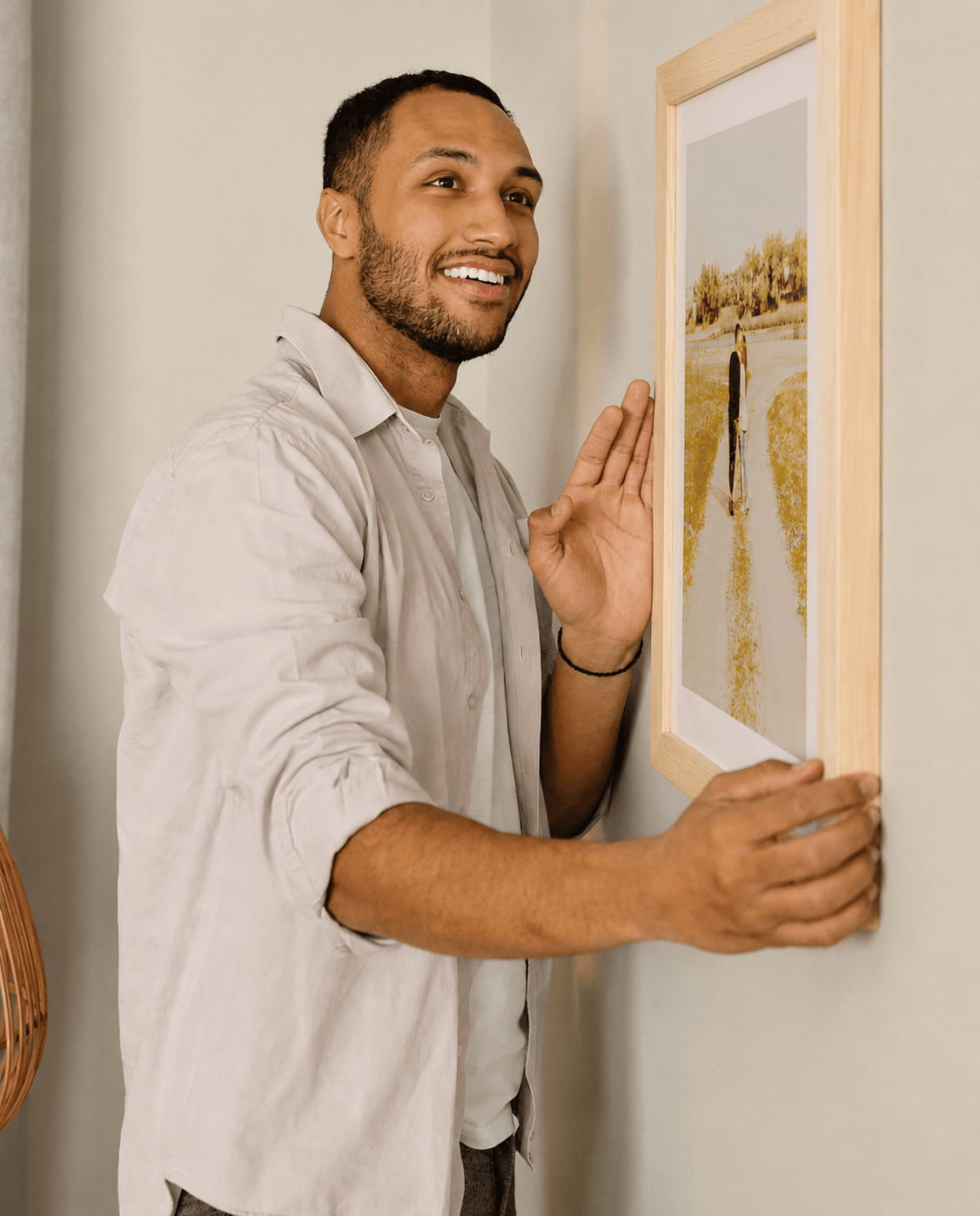 Man installing a maple wooden picture frame on a living room wall.