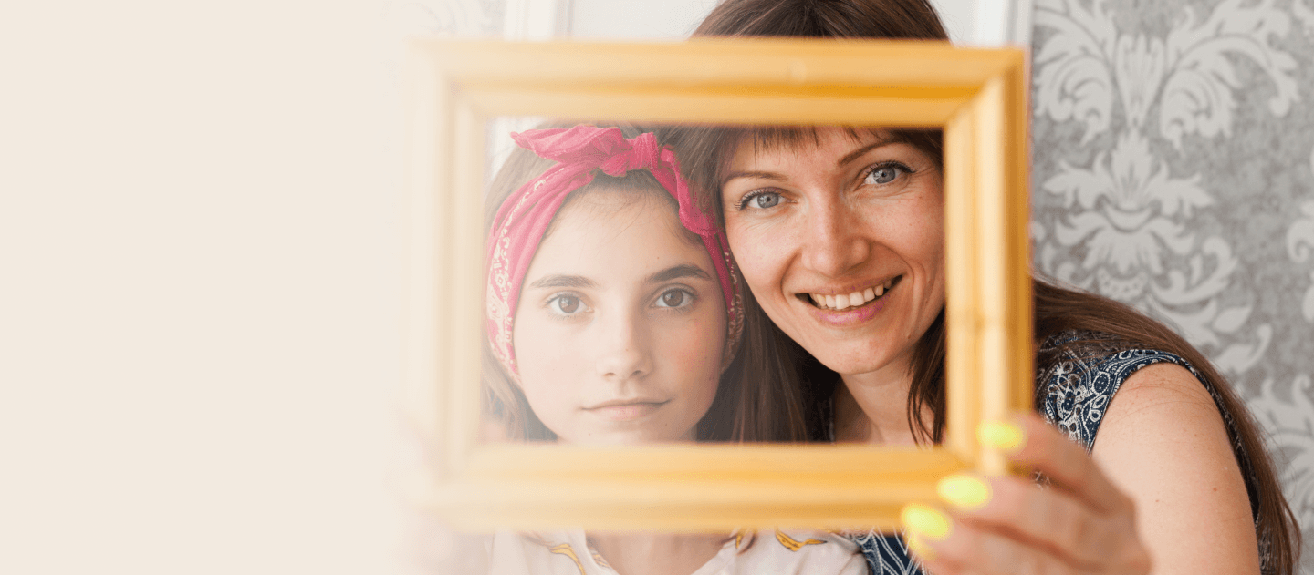 Mother and daughter smiling through a wooden picture frame.