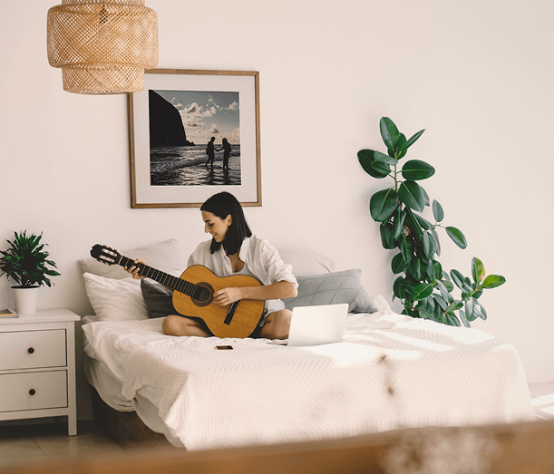 Woman playing guitar in a cozy bedroom with a framed photo print above the bed.